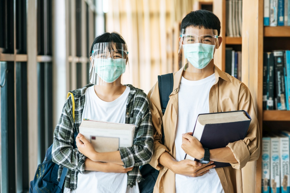 Men and women wear masks to stand to hold books in the library.