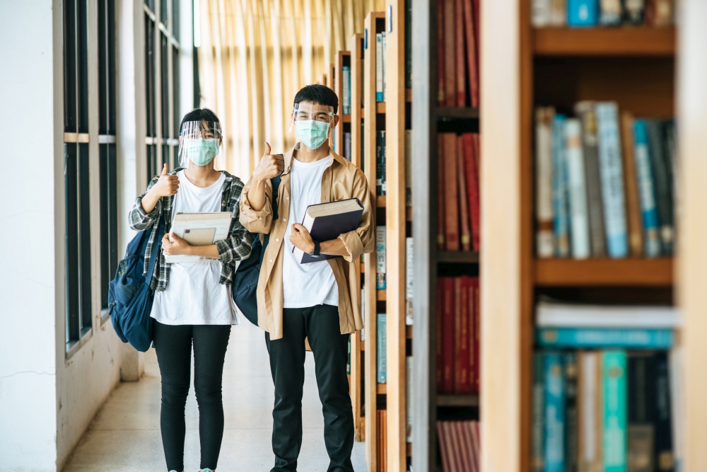 Men and women wear masks to stand, hold books in the library and put their thumbs up.