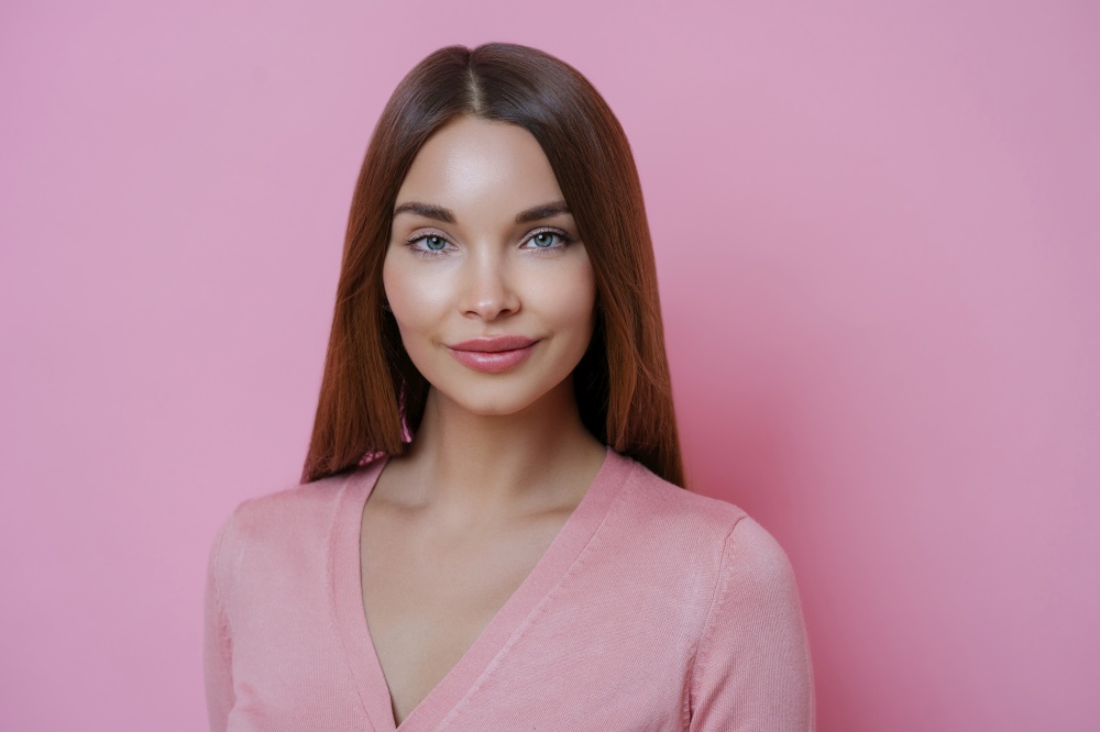 Portrait of good looking young European woman with long hair, has well cared complexion, dressed in casual clothes, isolated over pink background. People, face expressions and beauty concept.