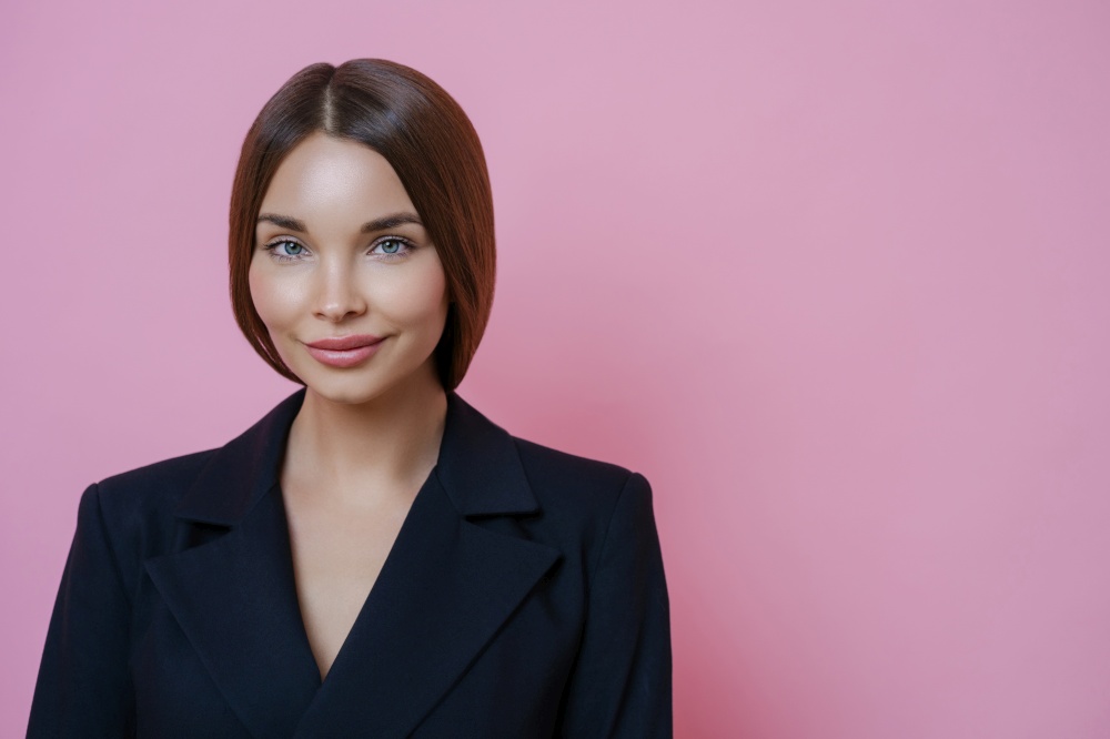 Delighted beautiful woman wears office clothes, has dark combed hair, introduces something to colleagues, isolated on pink background, blank space for your advertisement. Prosperous businesswoman
