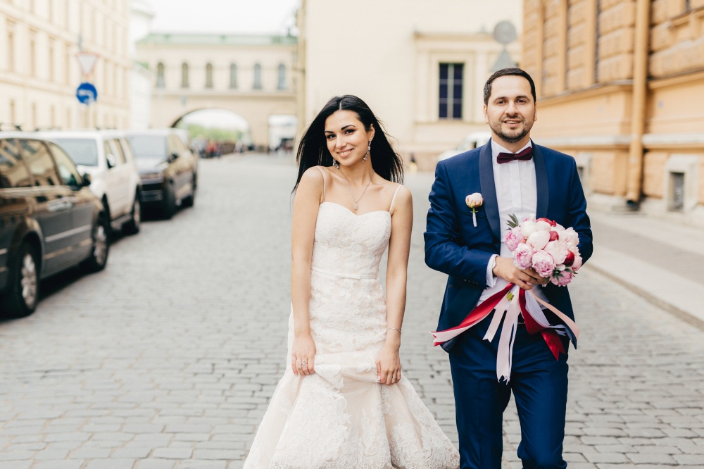 Bridegroom and bride have walk together, pose at camera, have pleased expressions, celebrate their wedding, being photographed for family album. Romantic happy young couple have special day.
