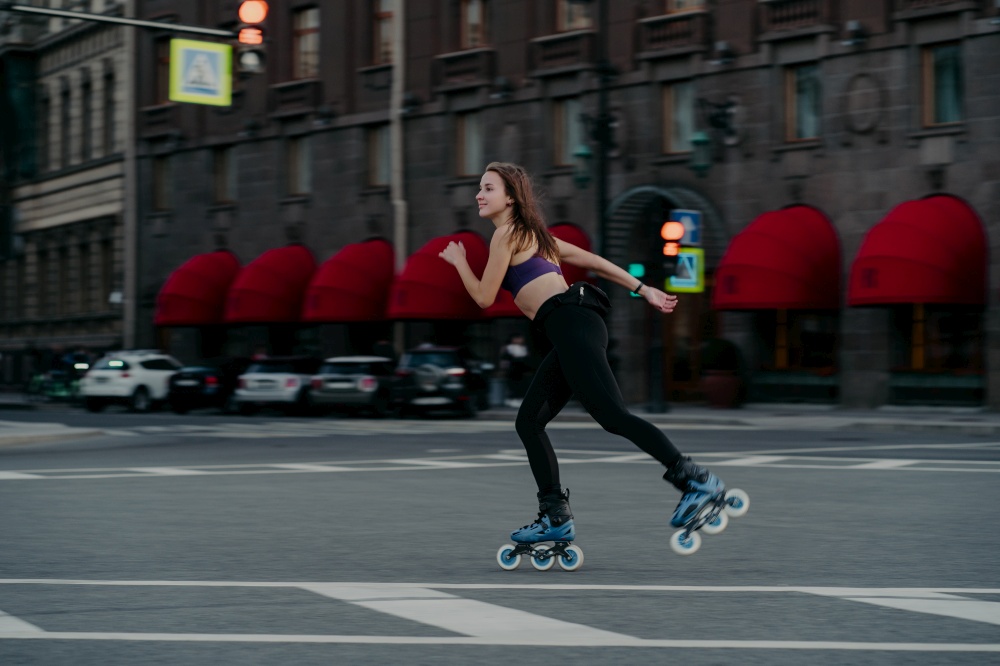 Extreme sport recreation and fitness activity concept. Active woman rides on rollers in urban environment strengthens leg muscles demonstrates high level of stability balances on small wheels