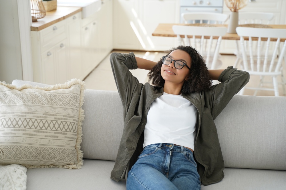 Lazy weekend morning. Attractive african american girl is relaxing on couch at home. Young woman is stretching, smiling and dreaming. Comfort and cosy home concept. Scandinavian interior.. Lazy weekend morning. Attractive african american girl is relaxing at home and smiling.
