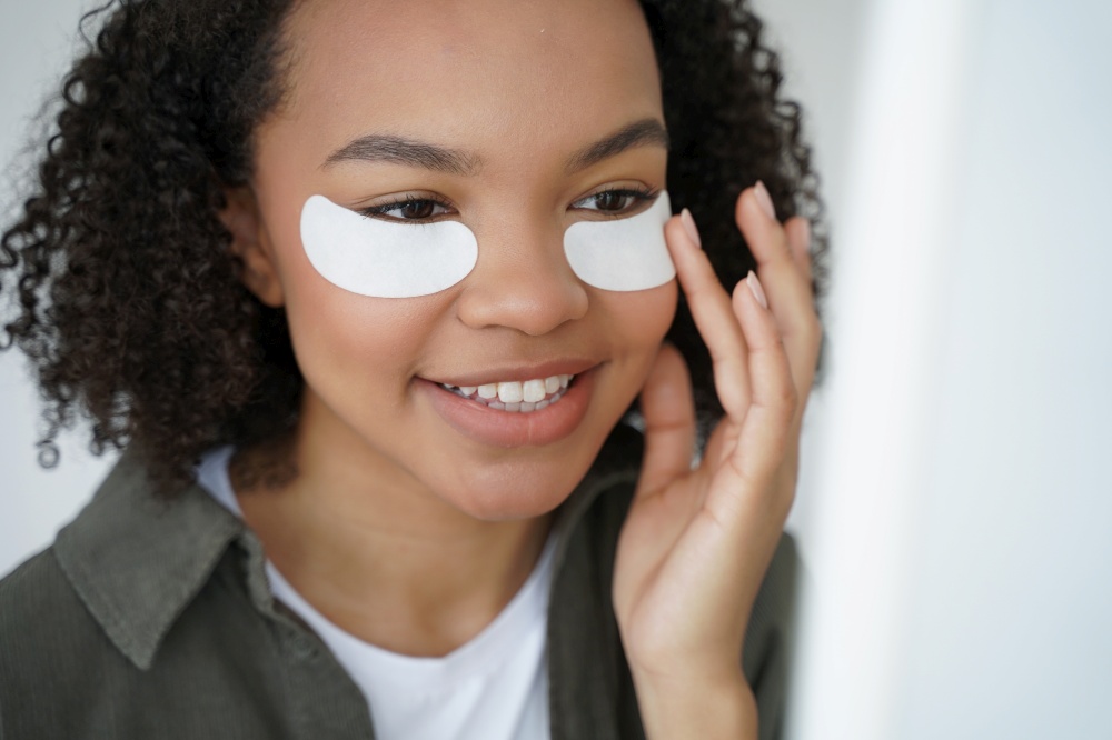 Young biracial girl use under eye patches, close-up portrait. Smiling pretty mixed race teen lady moisturize face by collagen pads for healthy facial skin. Skincare treatment, beauty routine.. Young biracial girl applying under eye patches for healthy fresh face skin. Skincare, beauty routine