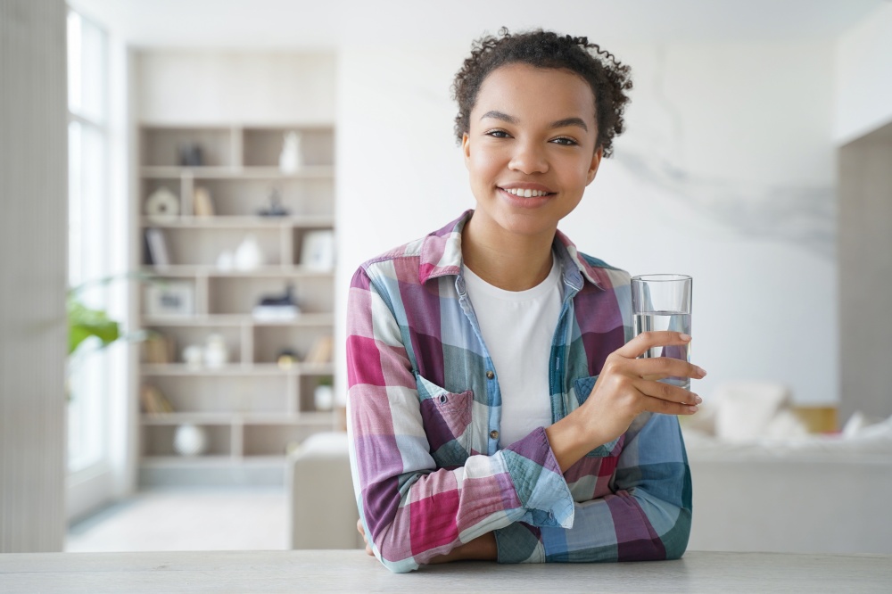 Happy african american girl drinks pure water from a glass. Gorgeous young woman has mineral water at home. Weight loss dieting, refreshing and detox. Healthy lifestyle, morning health routine.. Happy african american girl drinks water from a glass. Healthy lifestyle, morning health routine.