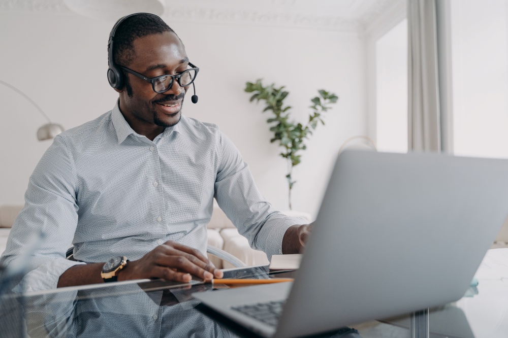 Online business talk. Afro american guy is speaking in front of camera. Happy businessman in formal wear and headset has online meeting in zoom. Manager of client support service has conversation.. Manager of client support service has conversation. Afro american guy speaking in front of camera.