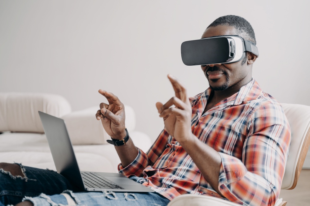 African american guy software delevoper wearing virtual reality glasses working in cyberspace at laptop. Modern black guy programmer freelancer developing programming VR game or application.. African american guy software delevoper in virtual reality glasses working in cyberspace at laptop