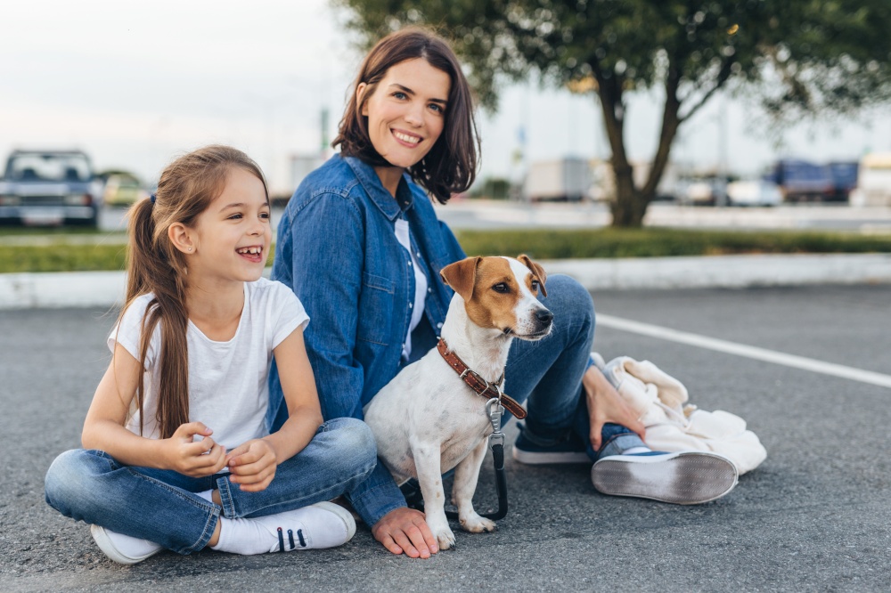 Content family of woman with pretty girl and adorable Jack Russell Terrier sitting on ground. . Happy mother with girl and dog