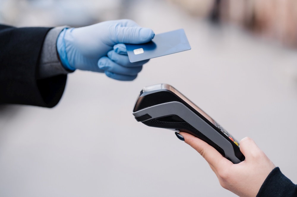 Faceless human in medical gloves during coronavirus epidemic, holds plastic card, tries to makes cashless payment for safety, uses modern technology. Pandemic, virus and prevention concept