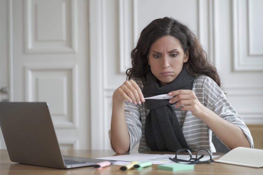 Sad unhealthy italian woman office worker feeling sick, looking at thermometer with worried face expression, measuring temperature at workplace, unhappy female employee with fever at work. Sad unhealthy italian woman office worker with thermometer feeling sick and unwell at workplace