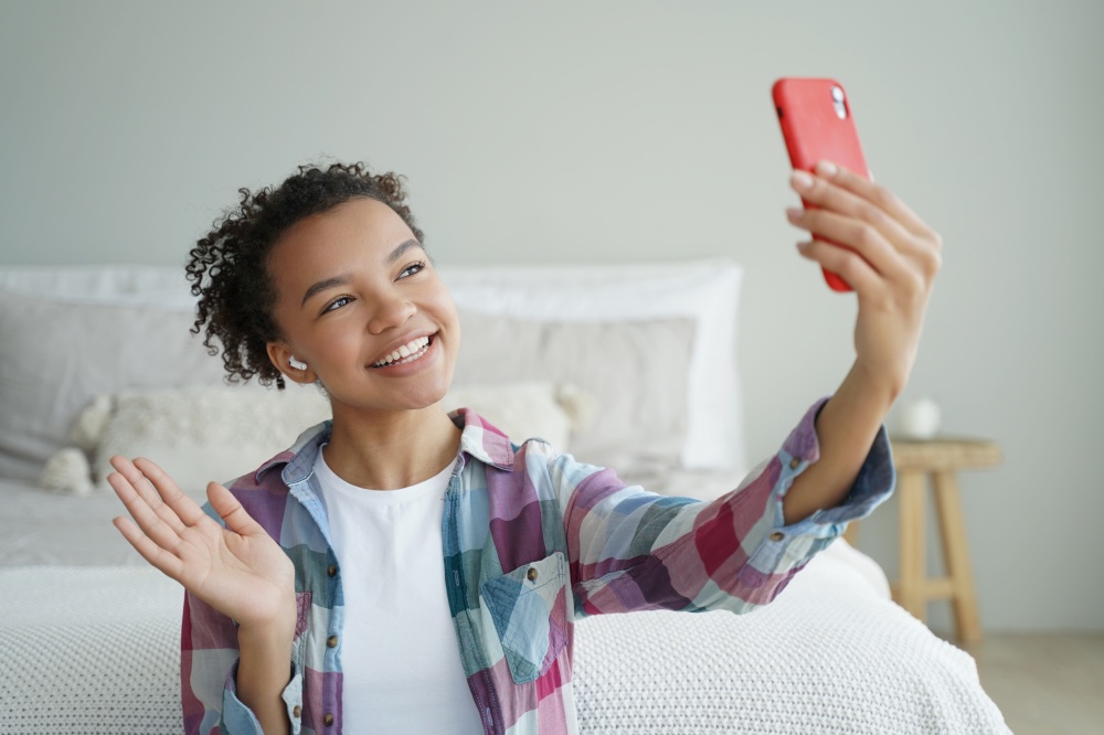 Video phone call. Curly african american woman is talking to friend on mobile phone. Young woman is speaking in front of camera and waving hand. Virtual communication concept. Teenage girl lifestyle.. Young woman speaking in front of camera and waving hand. Virtual communication concept.