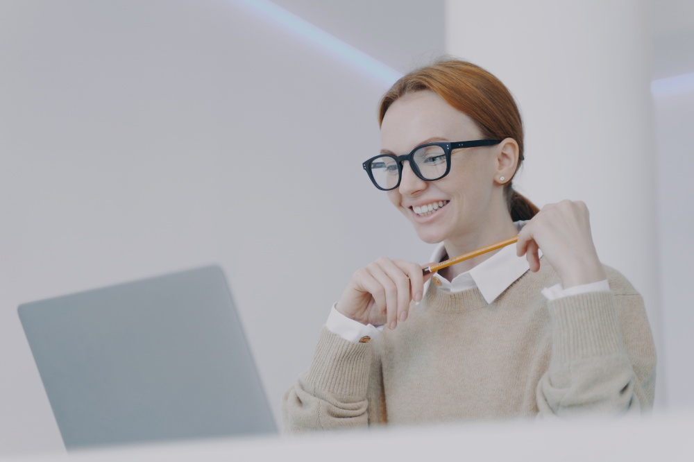 Young european businesswoman in glasses is happy. Secretary or manager at workplace in modern office. Successful attractive girl is studying at laptop. Positive female student.. Positive female student. Young european businesswoman in glasses is happy at workplace.