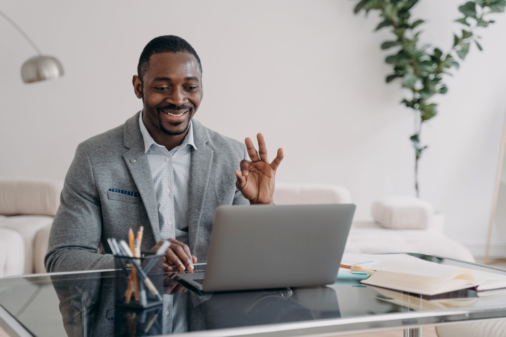 Smiling african american man talk by video call using laptop app agree with coworker, showing ok sign. Friendly black businessman freelancer show okay gesture to client, working online at distant job.. Smiling african american guy businessman show ok gesture talking by video call working at laptop