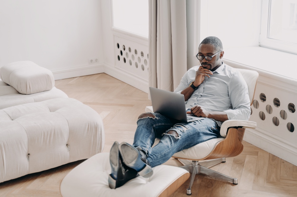 Confident professional at work in front of laptop. Relaxed african american businessman in formal wear is sitting in cosy chair at home. Online freelance job, startup project, remote work.. Confident professional at work in front of laptop. Relaxed african businessman in cosy chair.