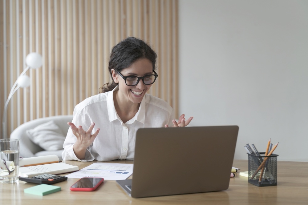 Overjoyed italian business woman reading great news on laptop at her workplace, happy female employee wearing glasses receiving good email, celebrating business success while sitting at office desk. Overjoyed italian businesswoman reading great news on laptop at her workplace