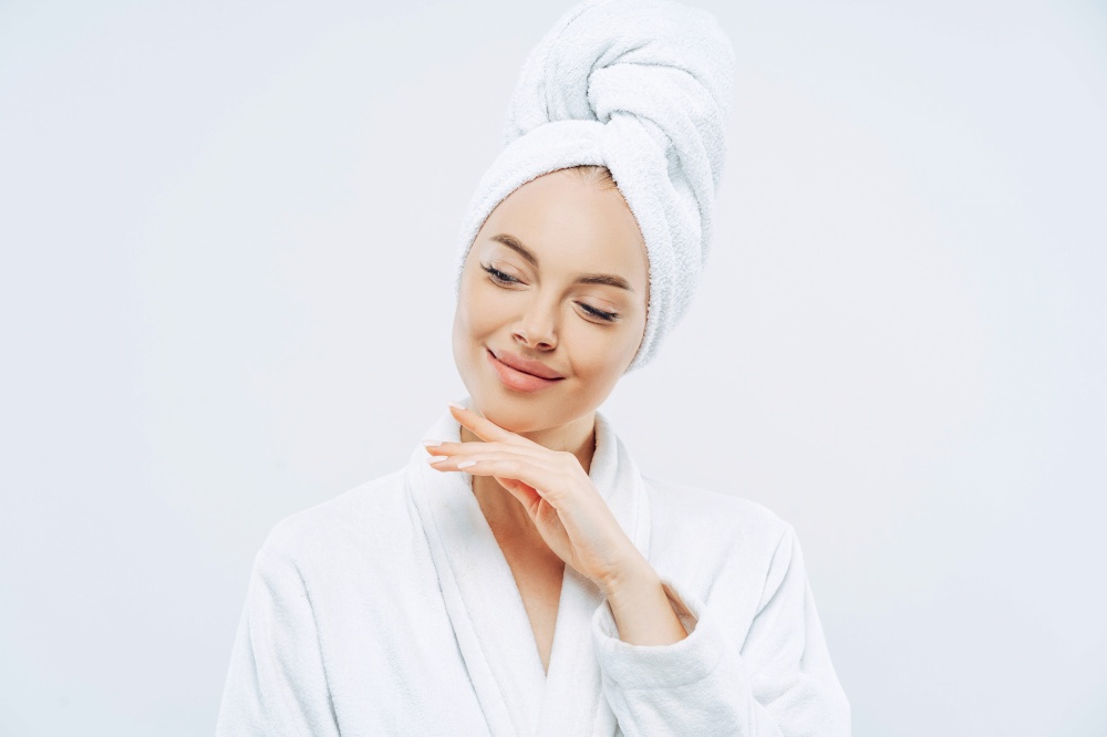 Natural woman touches jawline, towel on head, dries hair, cares for body, clean skin, prepares for party