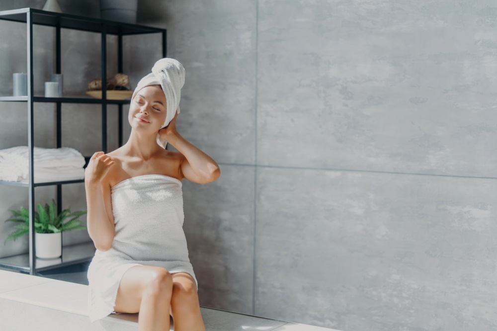 Refreshed Caucasian female model in towel on head, clean skin. Cozy bathroom pose. Women, beauty, hygiene.