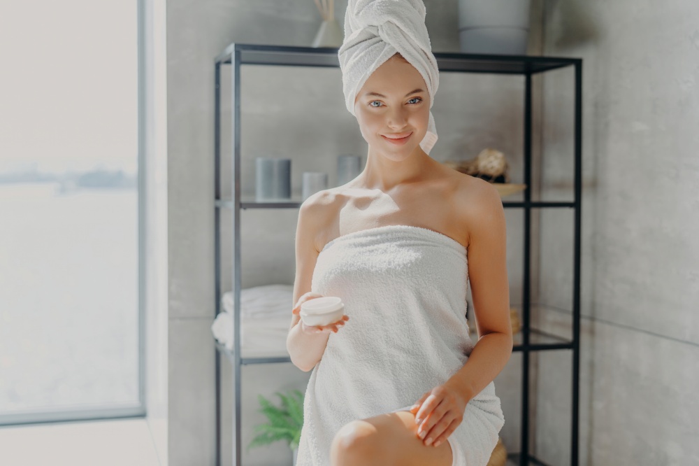 Pleased woman in towel, silky legs, smiling. Cosmetic product after shower, epilation. Moisturizing cream.