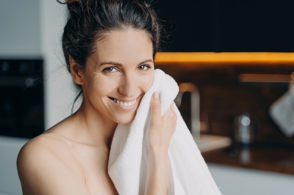 Caucasian woman smiling, drying face with towel. Daily shower, skincare routine. Hygiene, wellness, dermatology, cleansing.