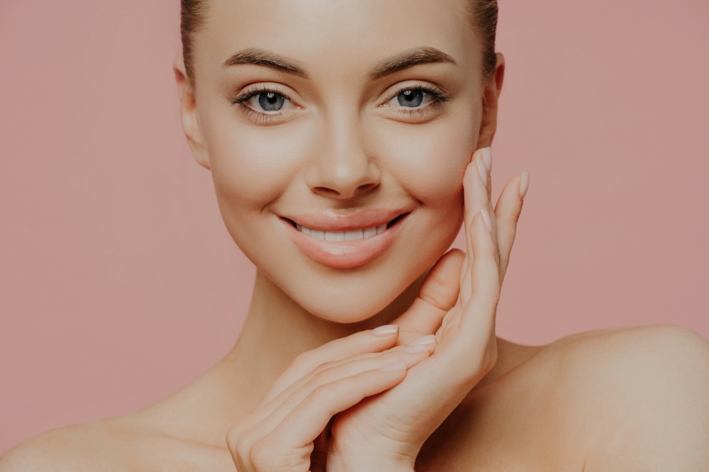 Close-up of woman with bare shoulders, touching face gently. Healthy skin, natural makeup, looking at camera. Beauty, face care, spa concept.