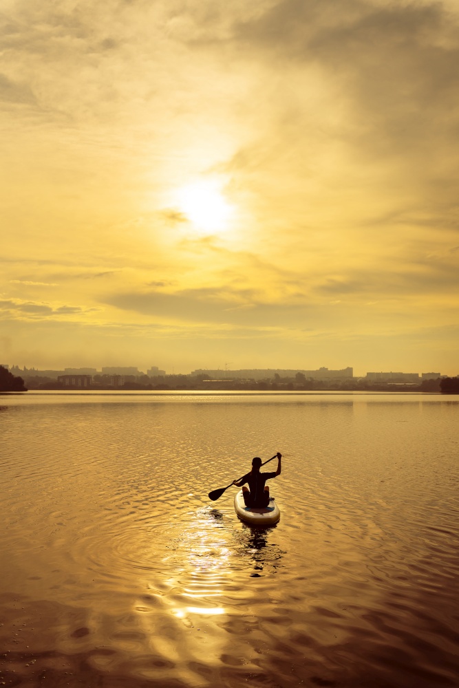 Stand up kayaking or stand-up paddleboarding on a quiet lake at sunset during a warm summer beach holiday, active woman. Stand up kayaking or stand-up paddleboarding on a quiet lake at sunset during a warm summer beach holiday, active woman.