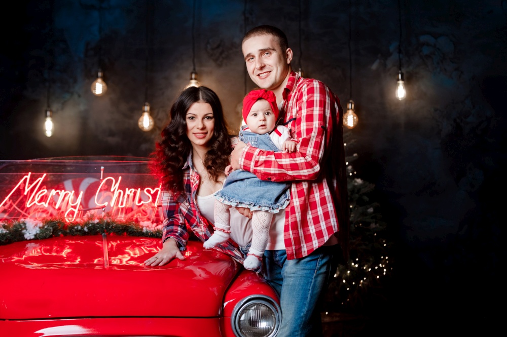 Young beautiful parents holding their little cute daughter in their arms having fun near retro car in studio. Christmas family look. New Year&rsquo;s scenery. Young beautiful parents holding their little cute daughter in their arms having fun near retro car in studio. Christmas family look. New Year&rsquo;s scenery.