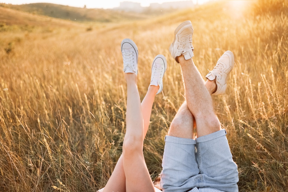 Woman and man having fun outdoors. Loving hipster couple are lying in the grass and lifting their legs in sneakers up in the summer at sunset light. valentines day. Woman and man having fun outdoors. Loving hipster couple are lying in the grass and lifting their legs in sneakers up in the summer at sunset light. valentines day.