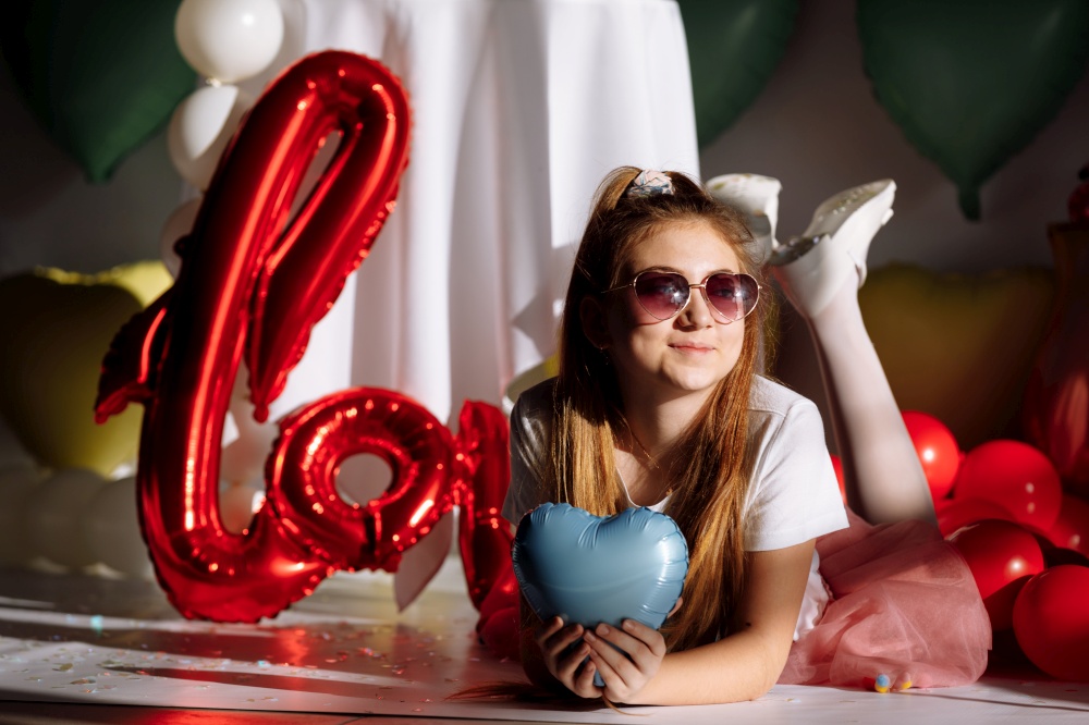 A happy bright girl in sunglasses in the shape of hearts with an inflatable balloon with the word Love. The concept of celebrating Valentine&rsquo;s Day. happy birthday party.. A happy bright girl in sunglasses in the shape of hearts with an inflatable balloon with the word Love. The concept of celebrating Valentine&rsquo;s Day. happy birthday party