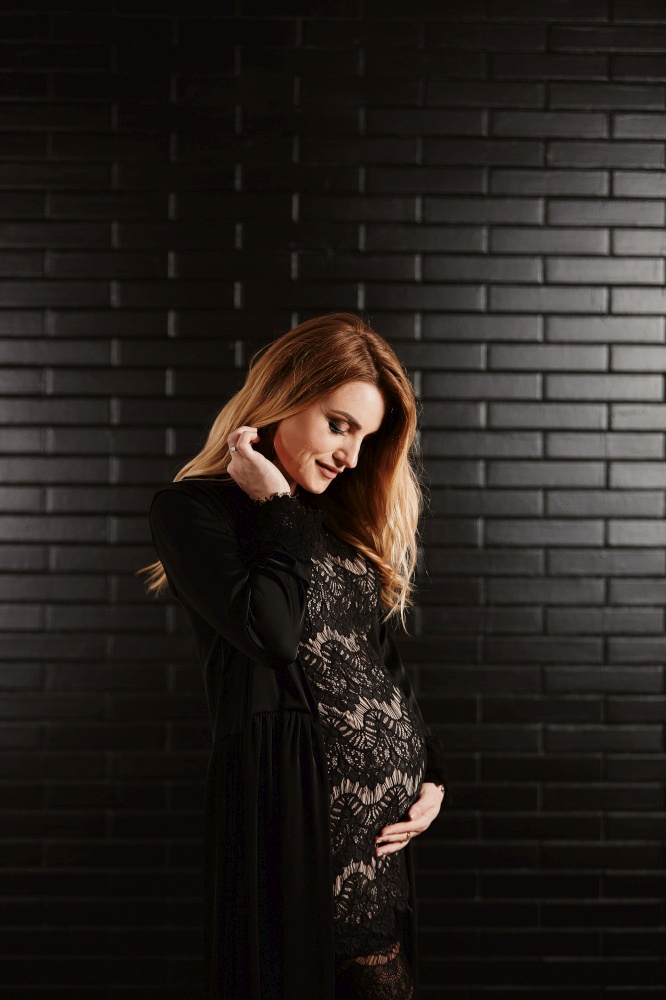 pregnant woman in black dress touching her belly on black brick wall. Motherhood, pregnant, people and expectation concept. Pregnant woman expecting baby. Maternity concept.. pregnant woman in black dress touching her belly on black brick wall. Motherhood, pregnant, people and expectation concept. Pregnant woman expecting baby. Maternity concept