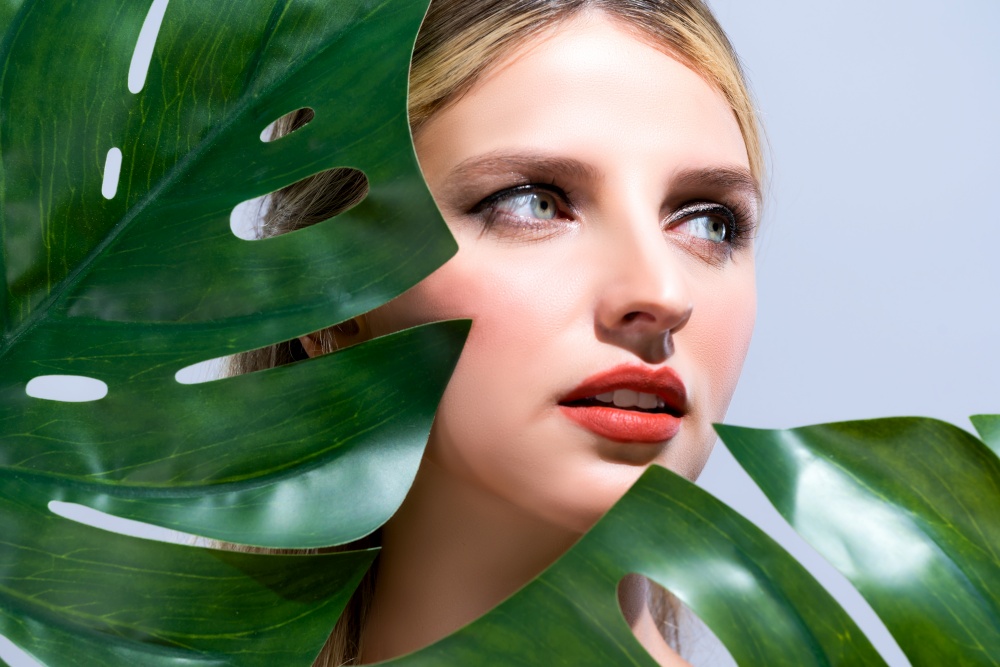 Closeup woman with perfect clean skin and alluring flawless natural soft facial makeup holding green leave monstera. Natural skincare treatment beauty or spa concept in isolated background.. Closeup woman with alluring perfect clean skin holding green leave.