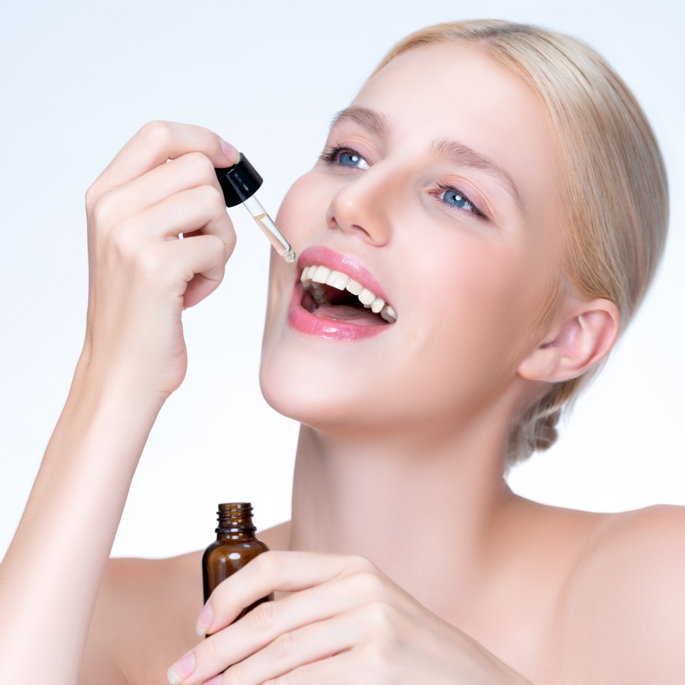 Closeup personable portrait of beautiful woman applying essential oil bottle for skincare product. Cannabis extracted CBD oil dropper for treatment and cannabinoids concept in isolated background.. Closeup personable beautiful woman holding CBD oil in isolated background.