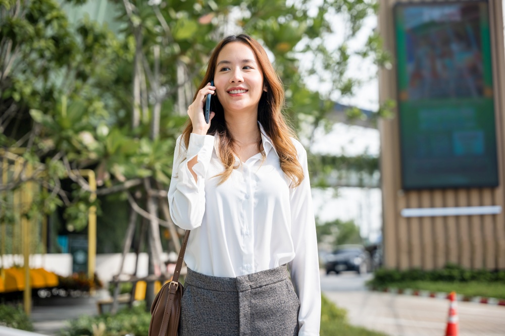 Asian business female calling on smart mobile phone and walking on street outside office building, Happy businesswoman talking on smartphone outdoor in city with client, business communication