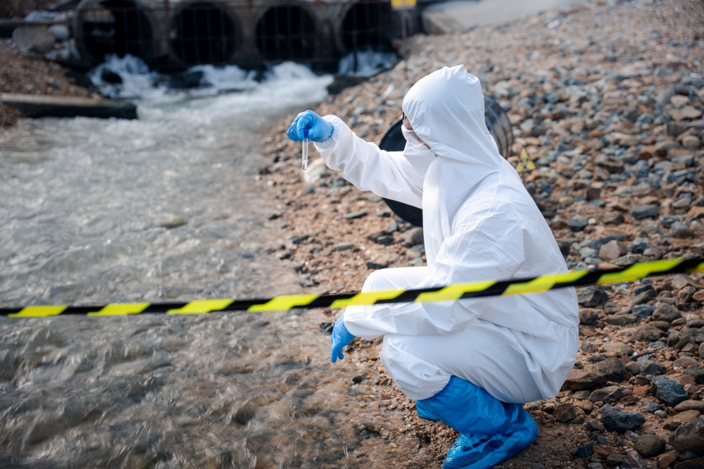 Ecologist sampling water from the river with test tube, Scientist or Biologist in a protective suit and protect mask collects sample of waste water from industrial for analyze, problem environment