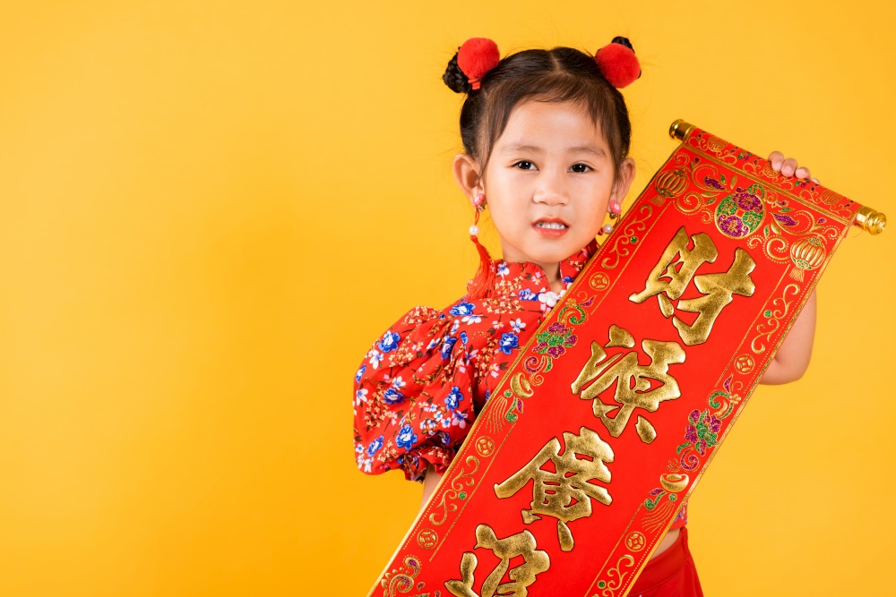 Chinese New Year. Happy Asian Chinese little child girl smile wearing red cheongsam qipao Spring festival couplets (Character "FU" means fortune, blessing), studio short isolated on yellow background