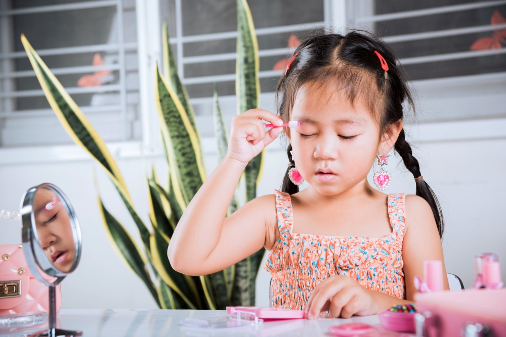 Asian adorable funny little girl making makeup her face she applying carborundum eyeliner to eyelid, Learning activity to be woman, happy kid is beautiful make up with cosmetics toy