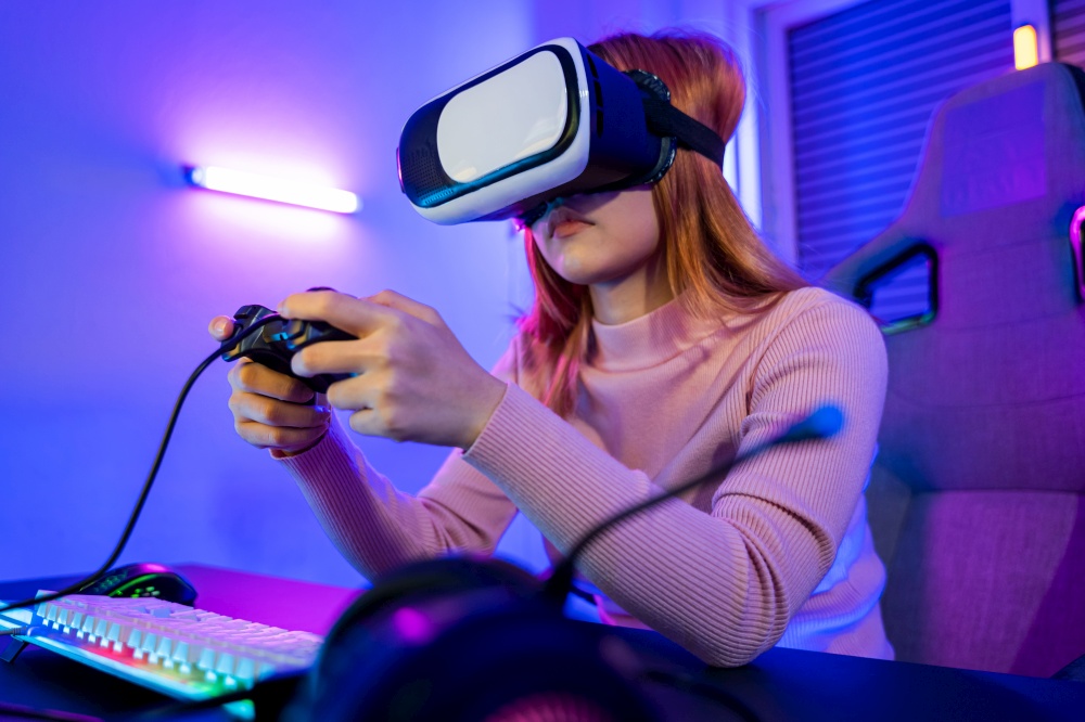 Excited woman virtual playing gamepad controller she very determined at home, Gamer in VR headset glasses exploring metaverse play video game online with joystick on computer neon lights