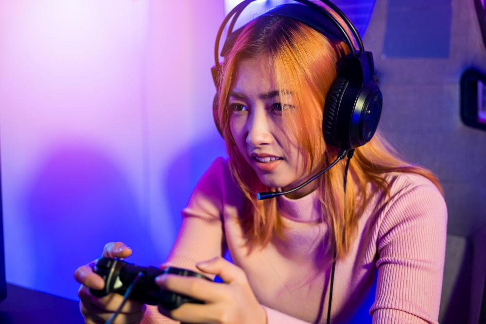 Gamer using joystick controller for virtual tournament plays online video game with computer neon lights, woman wear gaming headphones playing live stream esports games console at home, Esport concept