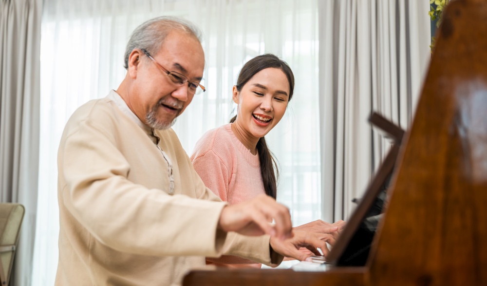 Family. Young woman teaching piano for senior man teaching, happy daughter and elderly father with eyeglasses relaxation playing piano together in living room at home, lifestyle life after retirement
