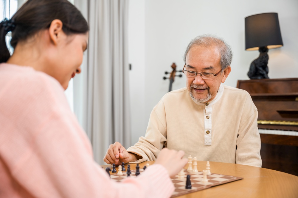 Smiling senior elderly having fun playing chess game with beautiful daughter at home, nurse caregiver in nursing home for leisure, Happy active retired people, Healthcare and medical homecare concept