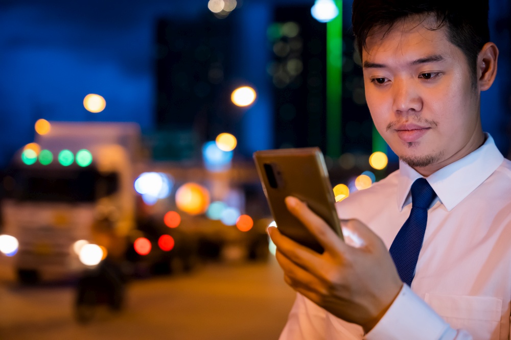 Young man walking and chatting on mobile phone with friends at social networks outdoor, Portrait Asian businessman typing an sms message via smartphone after work near office at night city street