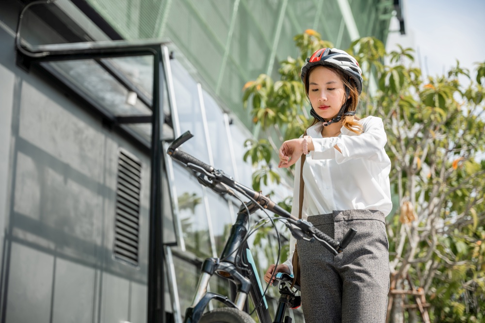 Portrait smiling woman checking watch, Asian young businesswoman standing with bicycle check clock time on urban city street in morning time go to work at office, Business commuter transportation
