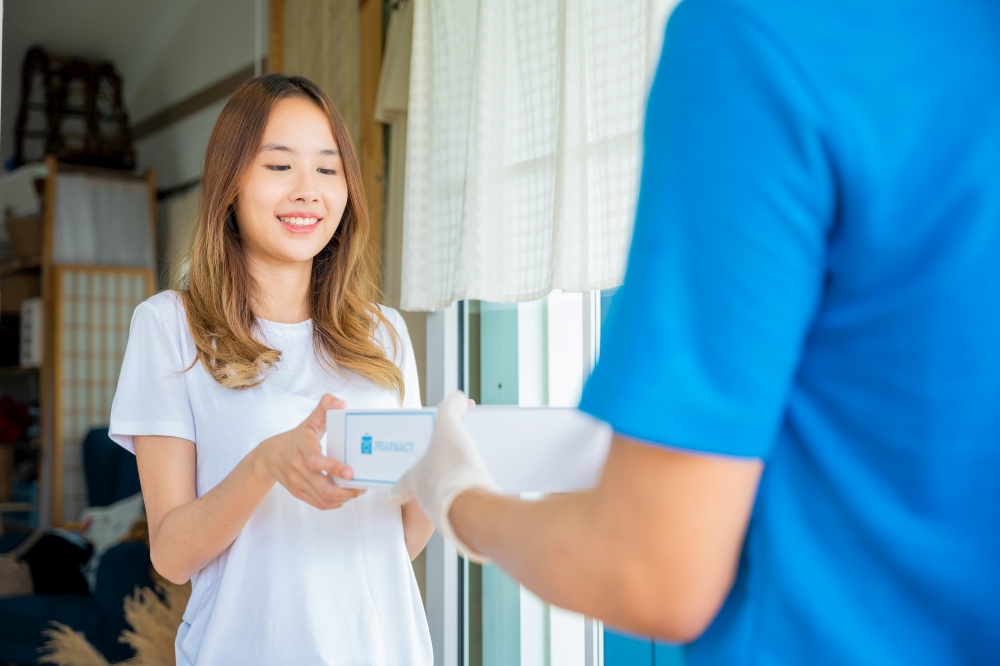 Sick Asian young woman receive medicine first aid pharmacy box from hospital delivery service, happy female receiving patient medicine drug from delivery man, healthcare medicine online concept