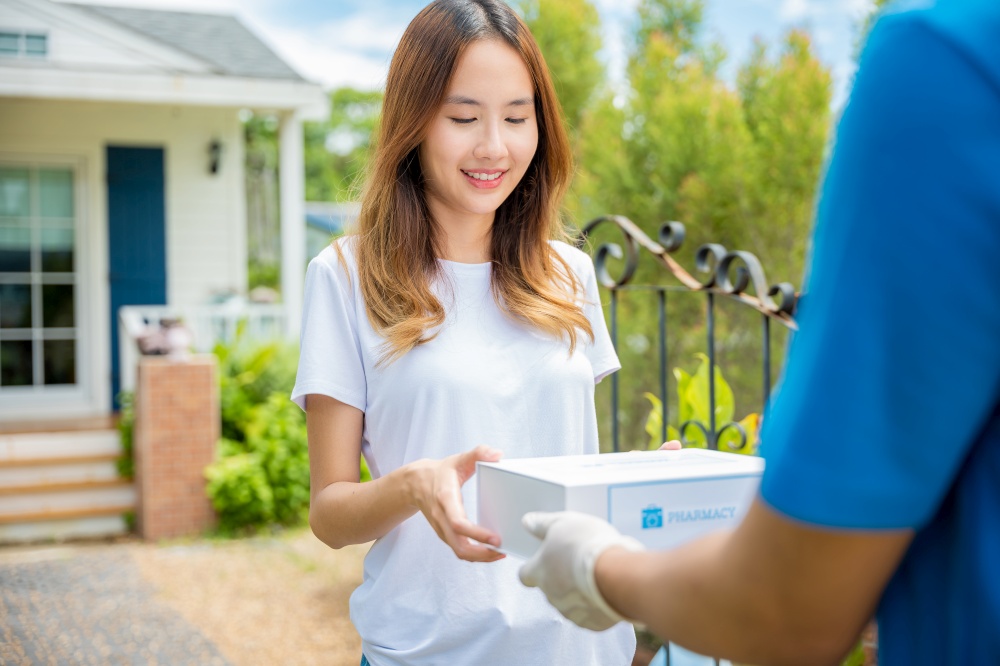 Delivery man give medicine drug to patient female at home, Sick Asian young woman receive medication first aid pharmacy box from hospital delivery service, healthcare medicine online concept