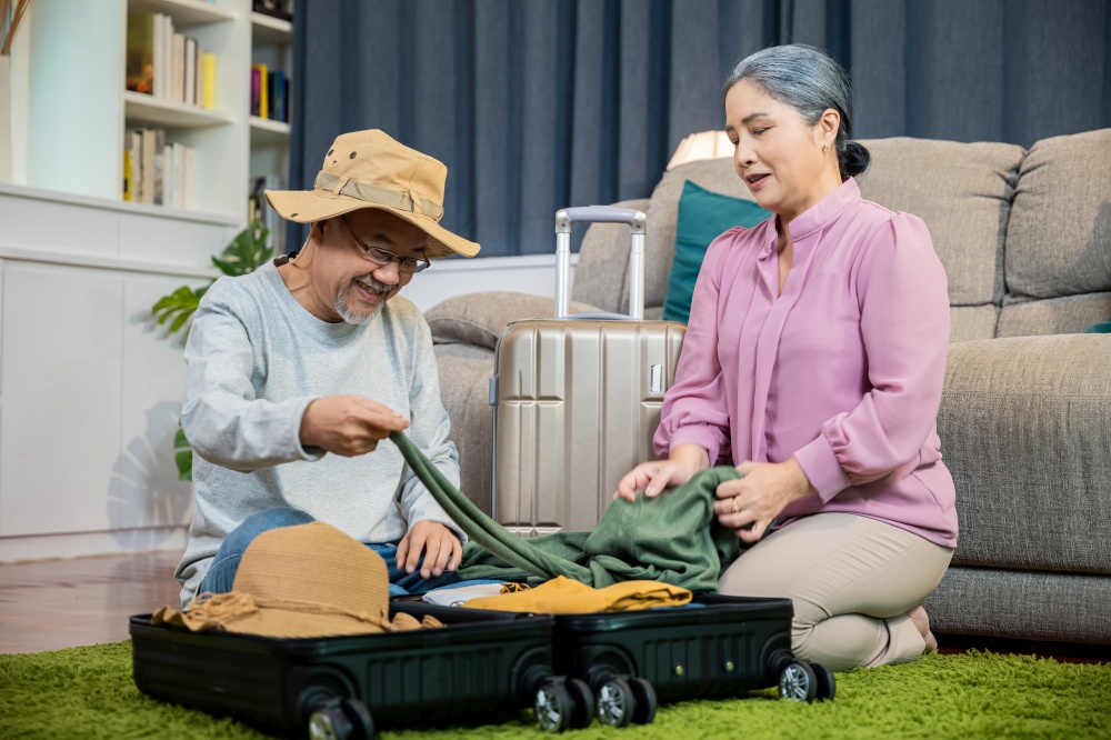 Asian couple old senior marry retired smiling prepare luggage suitcase arranging for travel, Romantic mature retired packing clothes travel bag suitcase together on floor at home for holiday