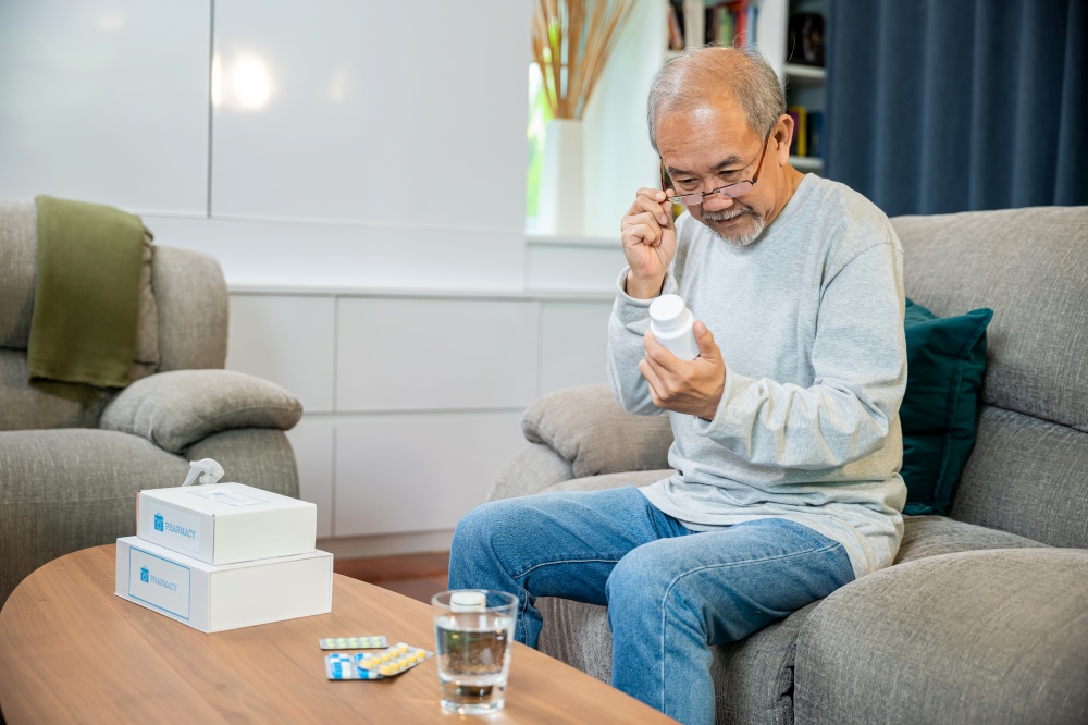 Asian worried senior man with medicine pills to taking on table in the living room, old man buy herbal self cure Rx pill online from pharmacy, home isolation, health care help service