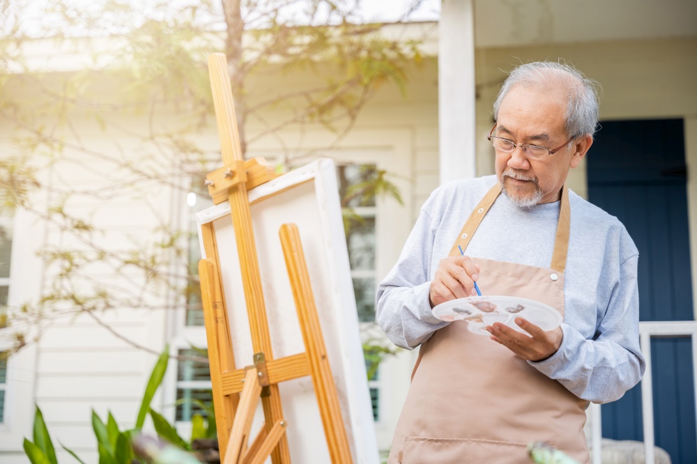 Artist. Asian senior old man painting picture using brush and oil color on canvas, lifestyle elderly people smile paint at his easel, Happy retirement and activity concept