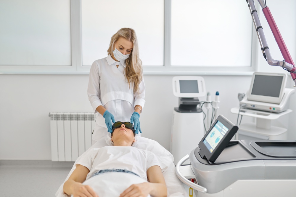 Cosmetician putting protective goggles on female client. Cosmetologist preparing client for facial laser carbon peeling procedure. Cosmetology and beauty concept. Cosmetologist preparing client for facial laser carbon peeling procedure