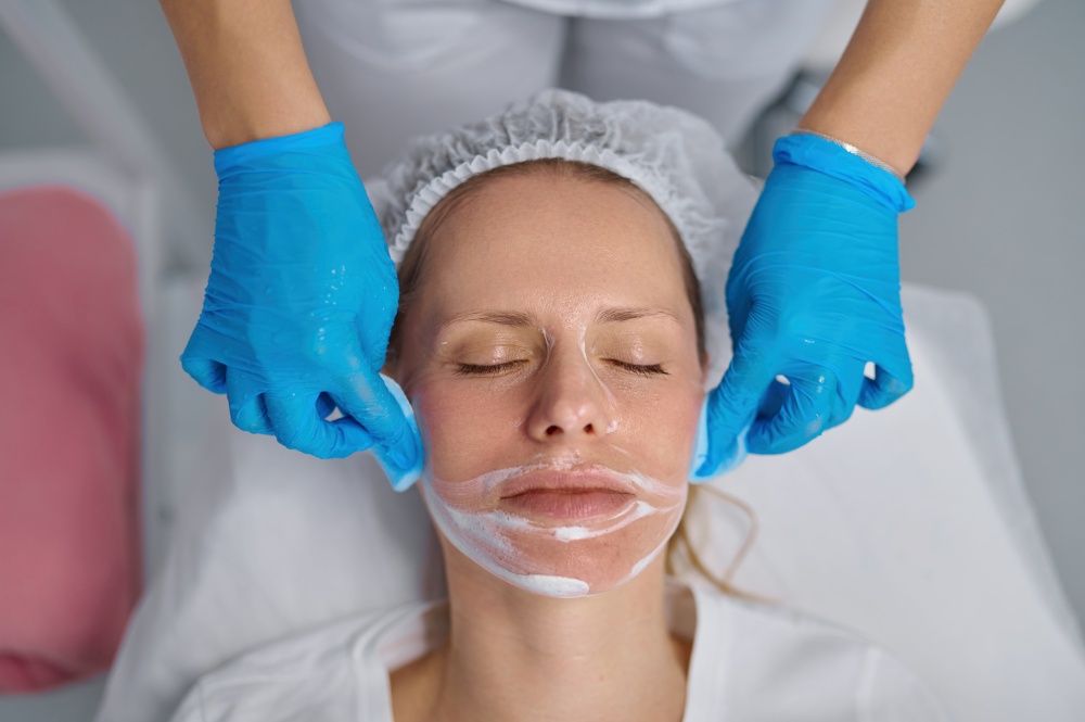 Beautician washes woman face using cotton pads to remove face mask. Facial cleansing procedure, cosmology service and beauty treatment concept. Beautician washes woman face using cotton pads to remove face mask