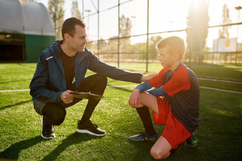 Young soccer coach giving support and advice to sad worry little football player. Coach talking putting hand on kid shoulder. Young soccer coach giving support to little football player