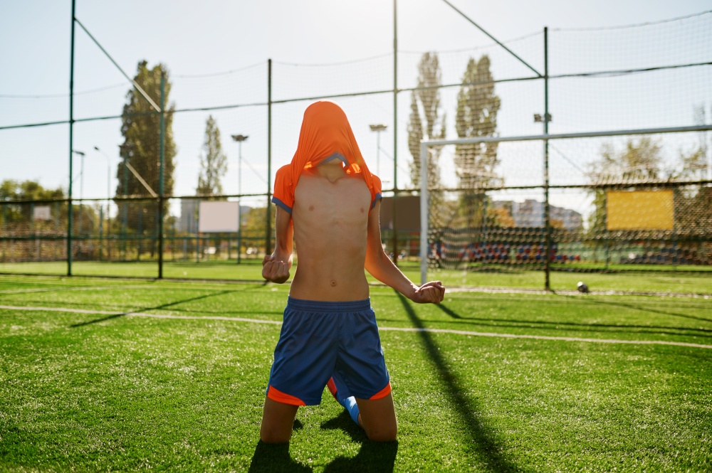 Emotional boy soccer player with t-shirt on head rejoicing goal or win showing yes gesture at stadium. Emotional boy soccer player with t-shirt on head rejoicing goal or win